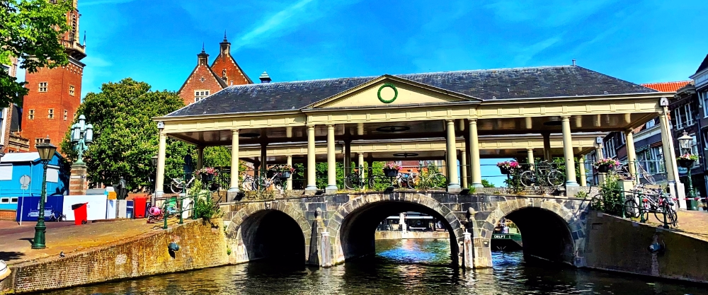 El histórico puente Koornbrug en Leiden, con su característica cubierta de madera y columnas, cruzando el canal bajo un cielo despejado.